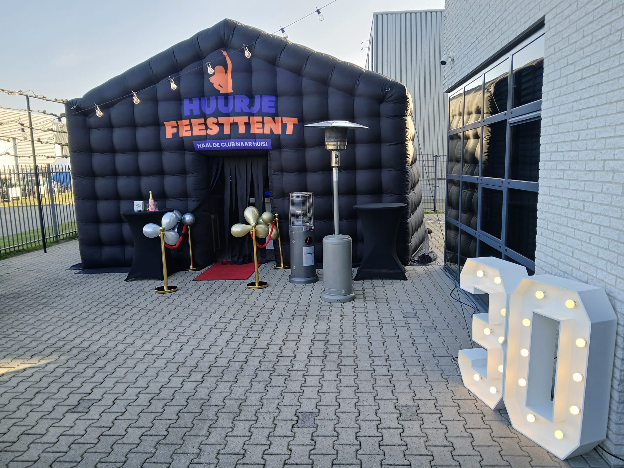 Drenthe - een luxe zwarte opblaasbare partytent op een parkeerplaats met twee lichtcijfers