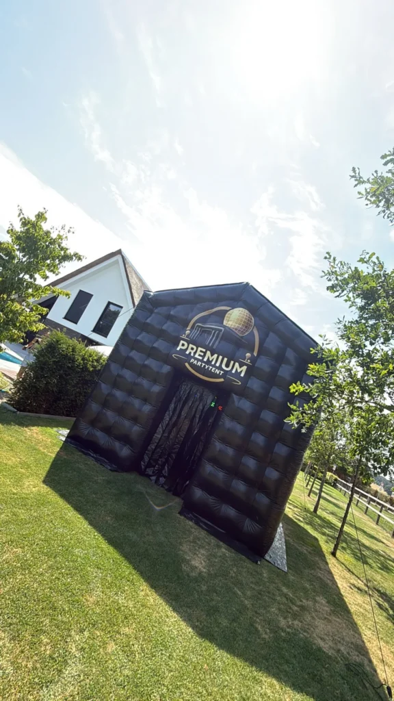 Opblaasbare partytent op een gazon bij een woonhuis onder een blauwe lucht